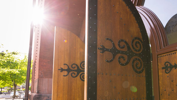 Close-up detail image of the arched wooden doors of the Red Gym,
with ornate decorative hinges, swung open with the sun shining in the background